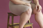 Close-up of a woman's leg sitting on a wooden stool against a pink background, illustrating body composition awareness and health.