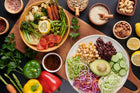 Colorful array of fresh vegetables and healthy ingredients laid out on a wooden board, featuring greens, tomatoes, avocados, beans, and nuts, perfect for a nutritious meal.