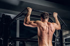 A man performing a pull-up on a gym bar, showcasing strong upper body muscles and proper form as he pulls himself upward.