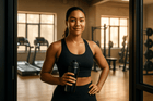 Confident woman in a black workout outfit holding a water bottle in a gym setting, ready for a workout.