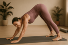 Woman practicing yoga in downward dog pose, showing signs of discomfort and strain in a modern studio setting with plants.