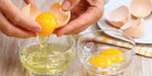 Hands cracking open a brown egg, separating the yolk from the egg whites into two glass bowls on a kitchen countertop.