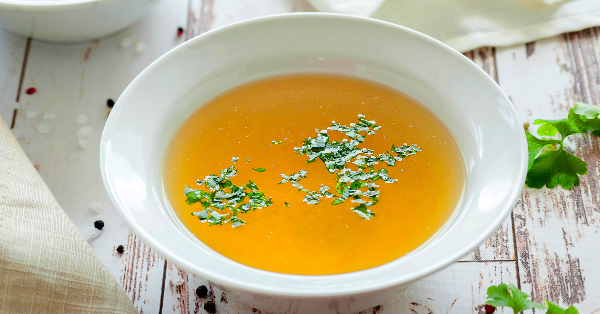 An image showing a bowl of bone broth with fresh herbs.