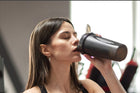 Woman enjoying a protein shake after workout in a gym setting, emphasizing a healthy lifestyle and fitness journey.