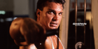 A focused bodybuilder performing a cable exercise in a gym, showcasing strength and determination, with sweat visible on his face.