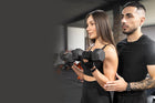 Fitness training session with a woman lifting dumbbells, guided by a male personal trainer, in a gym environment.